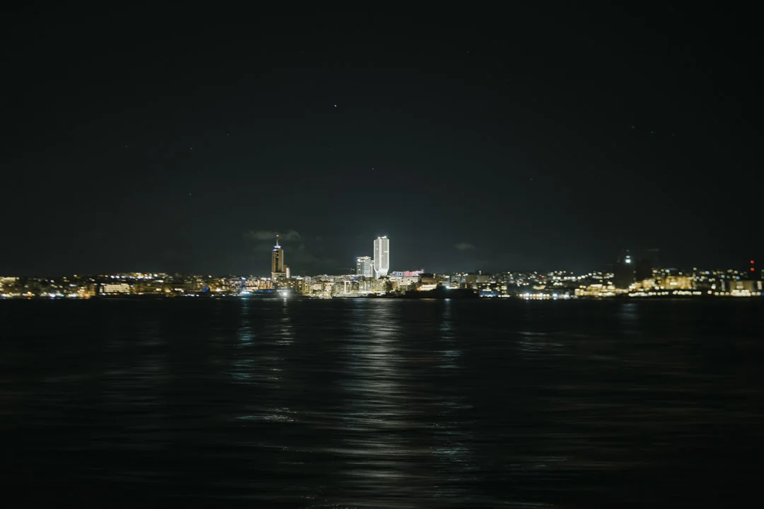 The illuminated coastline from the water · AFLOAT — Exclusive Networking at Sea